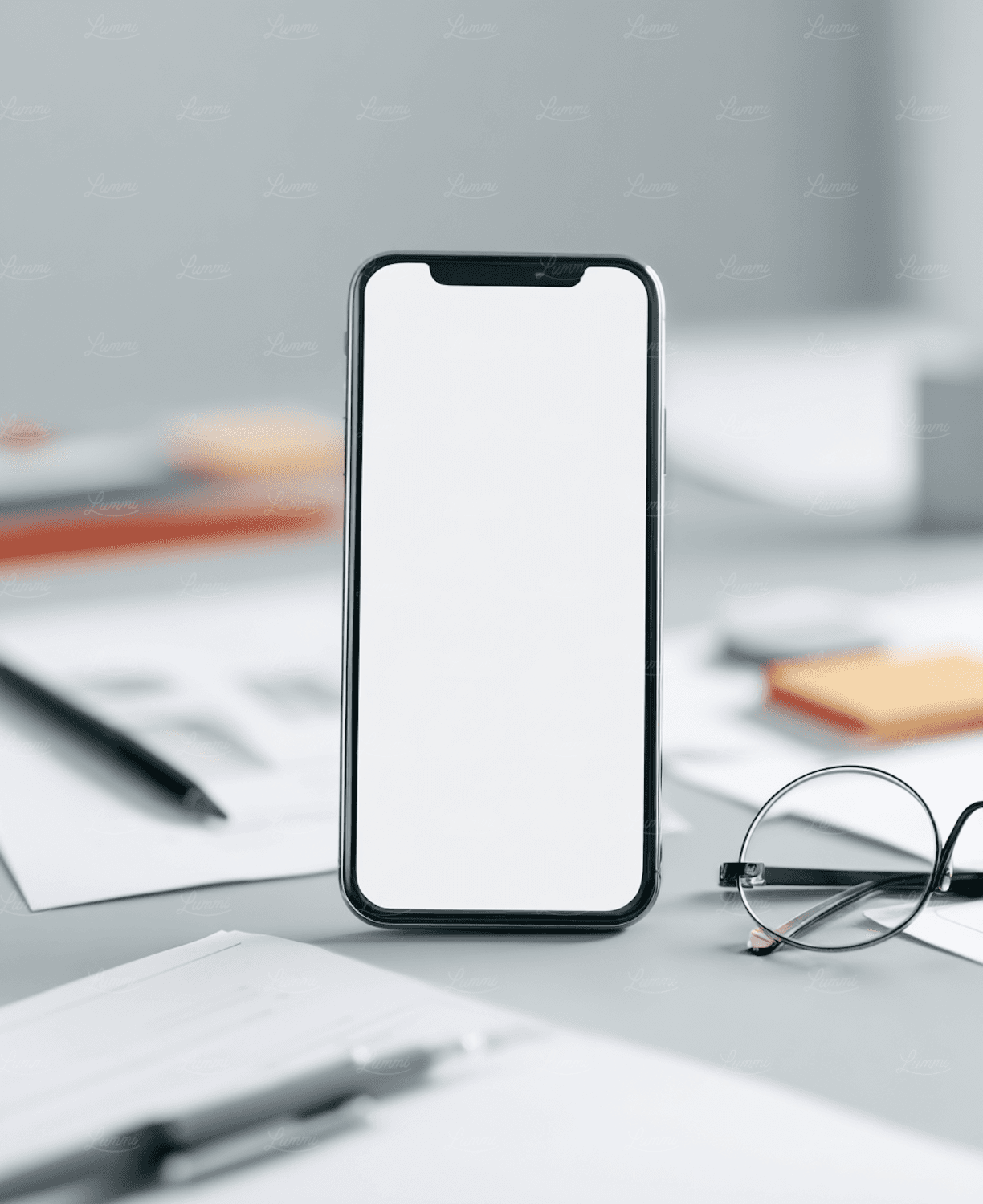 Smartphone auf einem Schreibtisch neben Brille, Papieren und Stiften